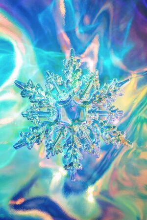 Clear glass snowflake on bright holographic background. Minimal christmas concept. Neon colors. Flat lay style.の写真素材