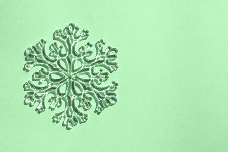Clear glass decorative snowflake in bright sunlight on trendy colored mint background. Minimal christmas concept. Copy space for text. Flat lay style.の写真素材