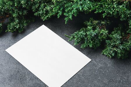 Empty white rectangle poster or card mockup on dark gray textured background with border of fluffy green fir branches. Copy space for text, flat lay, isometric view. Open composition.の写真素材