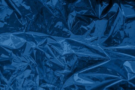 Abstract trendy dark blue colored crumpled foil texture background. 2020 color trend concept.