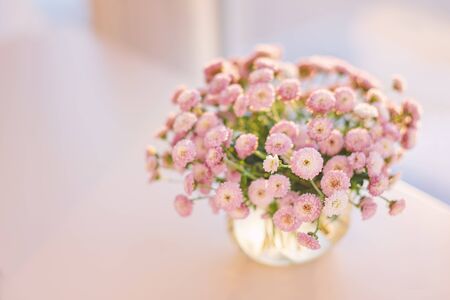 Close-up of small pink flowers bouquet in glass vase with blurred soft focused light background by the window. Slow living concept.の写真素材