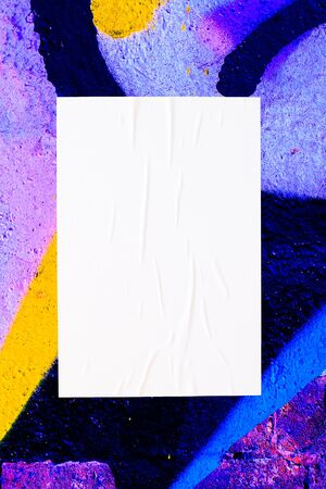 Closeup of colorful messy painted urban wall texture with wrinkled glued poster template . Modern...