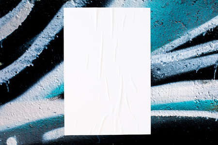 Closeup of colorful messy painted urban wall texture with wrinkled glued poster template . Modern...