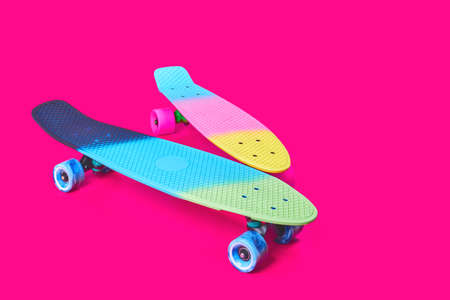 Two rainbow plastic Penny board skateboards on crimson background