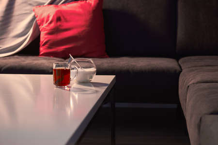 English tea In a dark room a sofa with a red pillow on the table a mug of tea