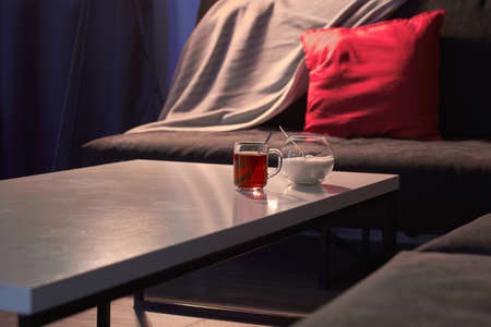 In a dark cozy room a sofa with a red pillow on the table a mug of teaの写真素材