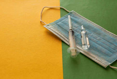 In the photo is a medical mask, a syringe for injection and an ampoule. The concept of vaccination of the populationの写真素材