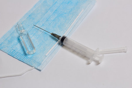 In the photo, the color background on it is a medical mask, a syringe and an ampoule. The concept of vaccination of the populationの写真素材
