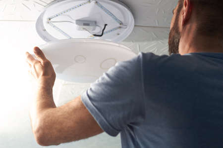 electrical technician changes the LED lamp on the ceiling, saving electricity.の写真素材