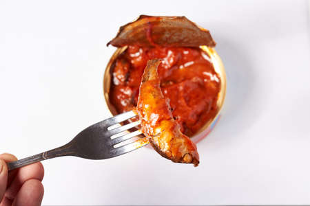Sprat in tomato sauce on a white background, fork with a hand. products.