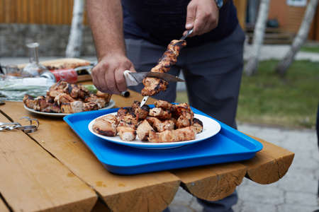 The cook removes the cooked shish kebab from the stick into a plate for serving for lunch.の写真素材