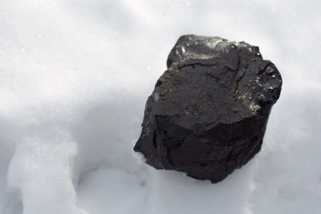 The black coal stone lying on the white snow symbolizes energy, warmth and wealth.の写真素材