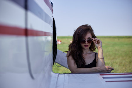 A gorgeous girl in sunglasses stands at the wing of a sports airplane sports and extreme.の写真素材