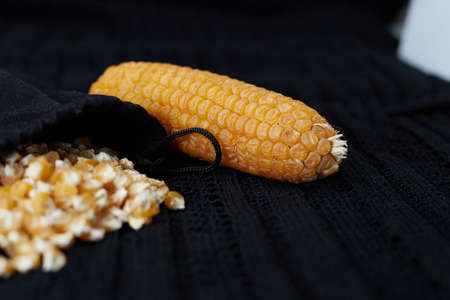 Yellow delicious corn seeds are lying in a bag next to a whole box on a black background.の写真素材