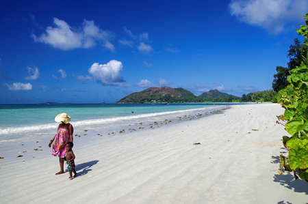 SEYCHELLES, PRASLIN - AUGUST 04: Women with child during walk along edge of ocean at Praslin island on August 04, 2015, Seychelles. Cote D'or Beach is considered to be the best beach on Praslin, Seychellesのeditorial素材