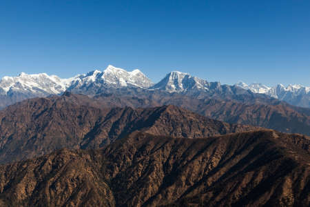 Beautiful mountain landscape with dark brown rocky mountains on the foreground and white snowy peak on the horizon and blue sky above them all. Himalayas, Neapal.の写真素材