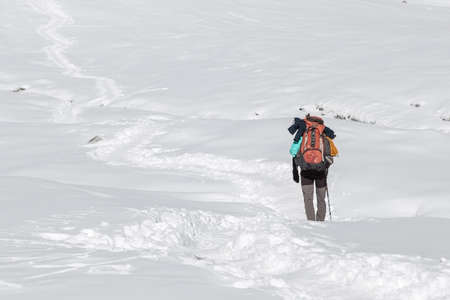 Extreme solo trekking concept. Single traveller walking in deep snow with big heavy backpack and...