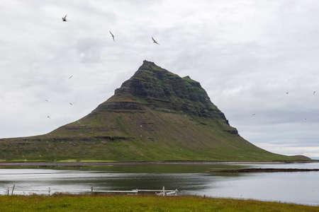 Famous Kirkjufell volcano reflected in water of the bay. Amazing green Icelandic mountain landscape...