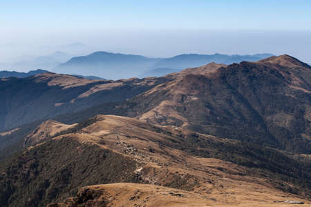Morning mountains misty landscape with dark green forest and brown dry grass on slopes. Dramatic hills scenery lit up by sun light and misty horizon in Nepal, Himalayas.の写真素材