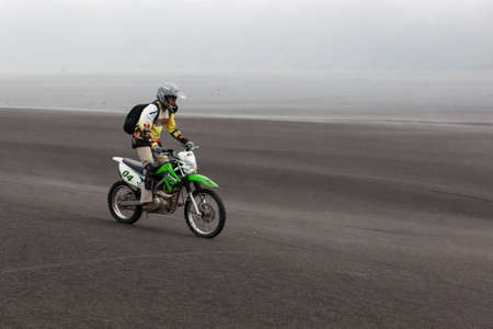 JAVA, INDONESIA - Apr 19, 2015: Tourist riding offroad bike through black ash sand dunes in Bromo...