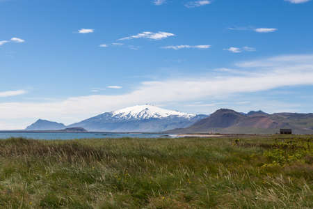 Beautiful Iceland landscape with white glacier cap of Snaefellsjokull volcano on the horizon. View from high green grass on the seashore across the bay. Rural landscape in western Iceland.の写真素材