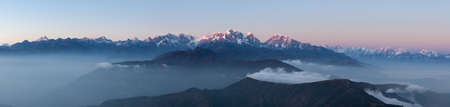 Panoramic mountain landscape with amazing clouds floating between hills on the sunrise. Himalayas panoramic mountain landscape with beautiful clouds flowing below high altitude snowy mountain peaks.の写真素材