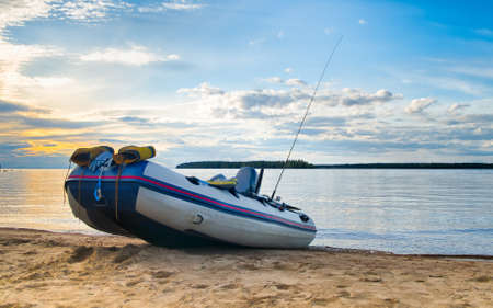 Inflatable fishing boat with fishing equipment on the lake coast line in the evening.の写真素材