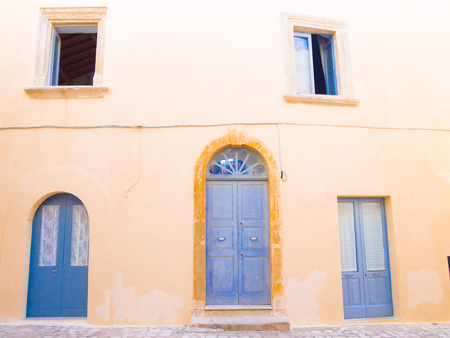 Otranto, Italy, Puglia, Old yellow facade with blue door and windows in old town center - Summer...