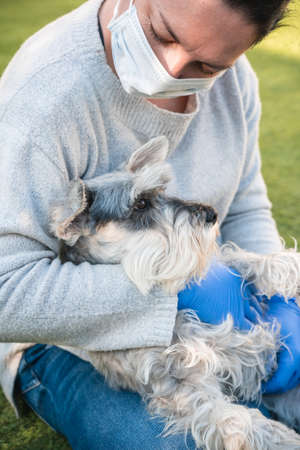 A woman protected with a procedure mask and blue medical gloves hugs and caresses a miniature...