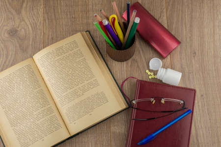 drowsiness and malaise at work: a box of pills to combat the drowsiness and weakness, glasses, a book and a Notepad, pencil case with pencils and pens, top viewの写真素材