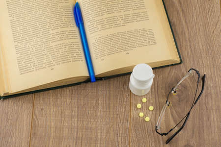 drowsiness and malaise at work: a box of caffeine pills, glasses, open book, blue pen - a view from above, closeの写真素材