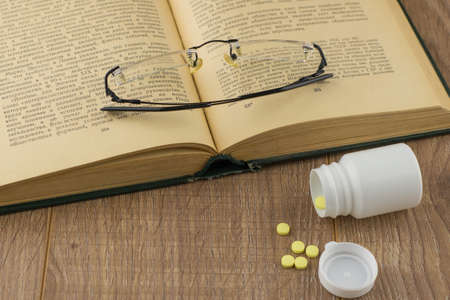 drowsiness and malaise at work: a box of pills to combat the drowsiness and weakness, glasses, open book top viewの写真素材