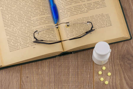 drowsiness and malaise at work: a box of caffeine pills, glasses, open book, blue pen - top viewの写真素材