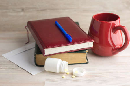 ensuring good employee: a pack of tablets of ephedrine, Cup of strong coffee. nearby are at wooden table on the envelope, a book, Notepad and blue penの写真素材
