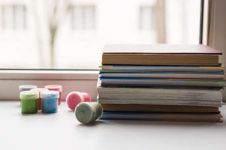 A stack of old various books and some color pencils lying on the windowsill, a few different gouache colors scattered nearbyの写真素材