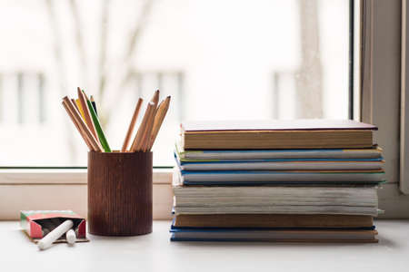 A stack of old books and several different colored pencils lie on the windowsill, a box of crayons lies on the sideの写真素材