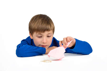 Origami: a schoolboy boy in a blue T-shirt sits at the table and plays with a paper bird, wants to feed herの写真素材