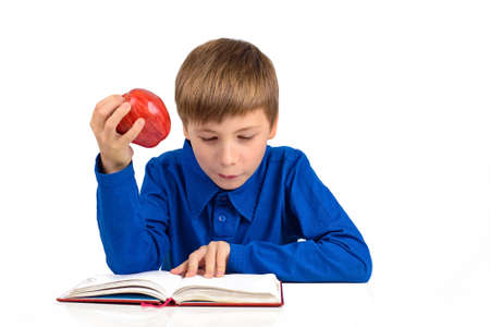 boy schoolboy in a blue t-shirt is preparing for school, reading something in a notebook, holding a red appleの写真素材