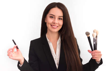 girl, makeup artist, with long dark hair in a business suit holding a brush and tweezers, on a white backgroundの写真素材