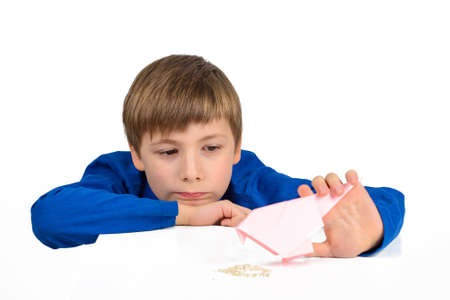 Origami: a schoolboy boy in a blue T-shirt sits at the table and plays with a paper bird, wants to feed herの写真素材