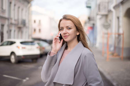 stylish girl with red hair calls by mobile phone on the city streetの写真素材