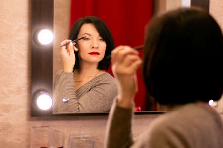 woman with black hair straightens makeup at the dressing table with a mirrorの写真素材