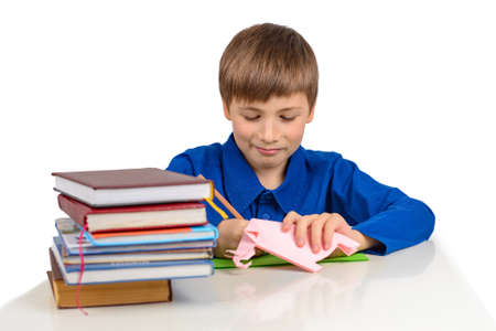 child development: a schoolboy boy in a blue T-shirt sits at the table and draws on colored paper, next to a stack of textbooks and paperwork, origamiの写真素材