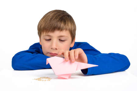 Origami: a schoolboy boy in a blue T-shirt sits at the table and plays with a paper bird, wants to feed herの写真素材