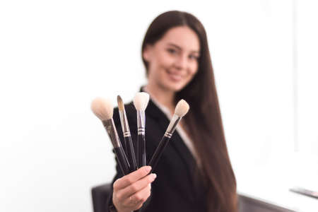 girl, makeup artist, with long dark hair in a business suit holding a brush on an outstretched hand, on a white backgroundの写真素材