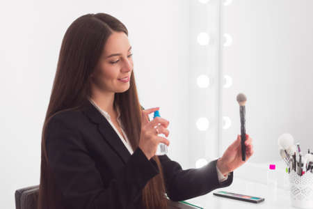 girl with long dark hair in a business suit sits at the make-up table and splashes liquid onto the brushの写真素材