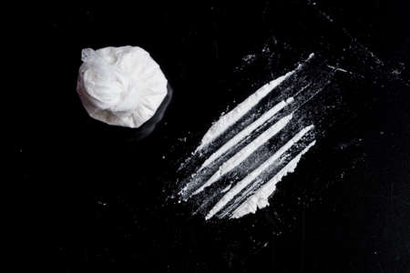 white powder (heroin, cocaine, narcotic) in a plastic bag on a black background, drugs are scattered in the form of a trackの写真素材