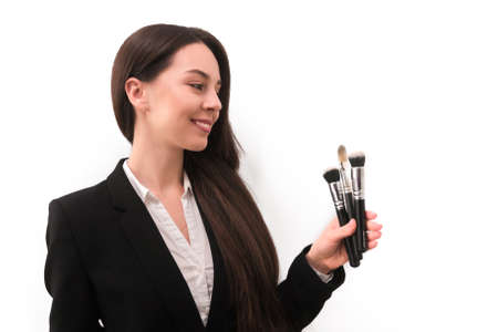 girl with make-up with long dark hair in a business suit holding a brush in his hand, on a white backgroundの写真素材