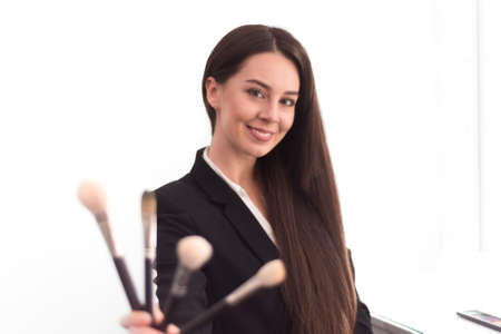 girl, makeup artist, with long dark hair in a business suit holding a brush on an outstretched hand,...