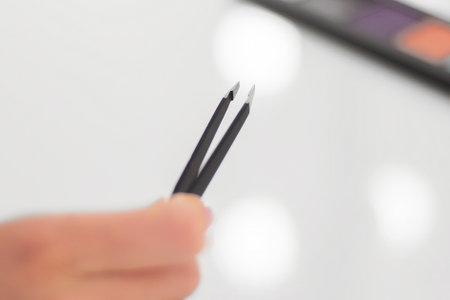 female hand holding eyebrow tweezers over the make-up tableの写真素材
